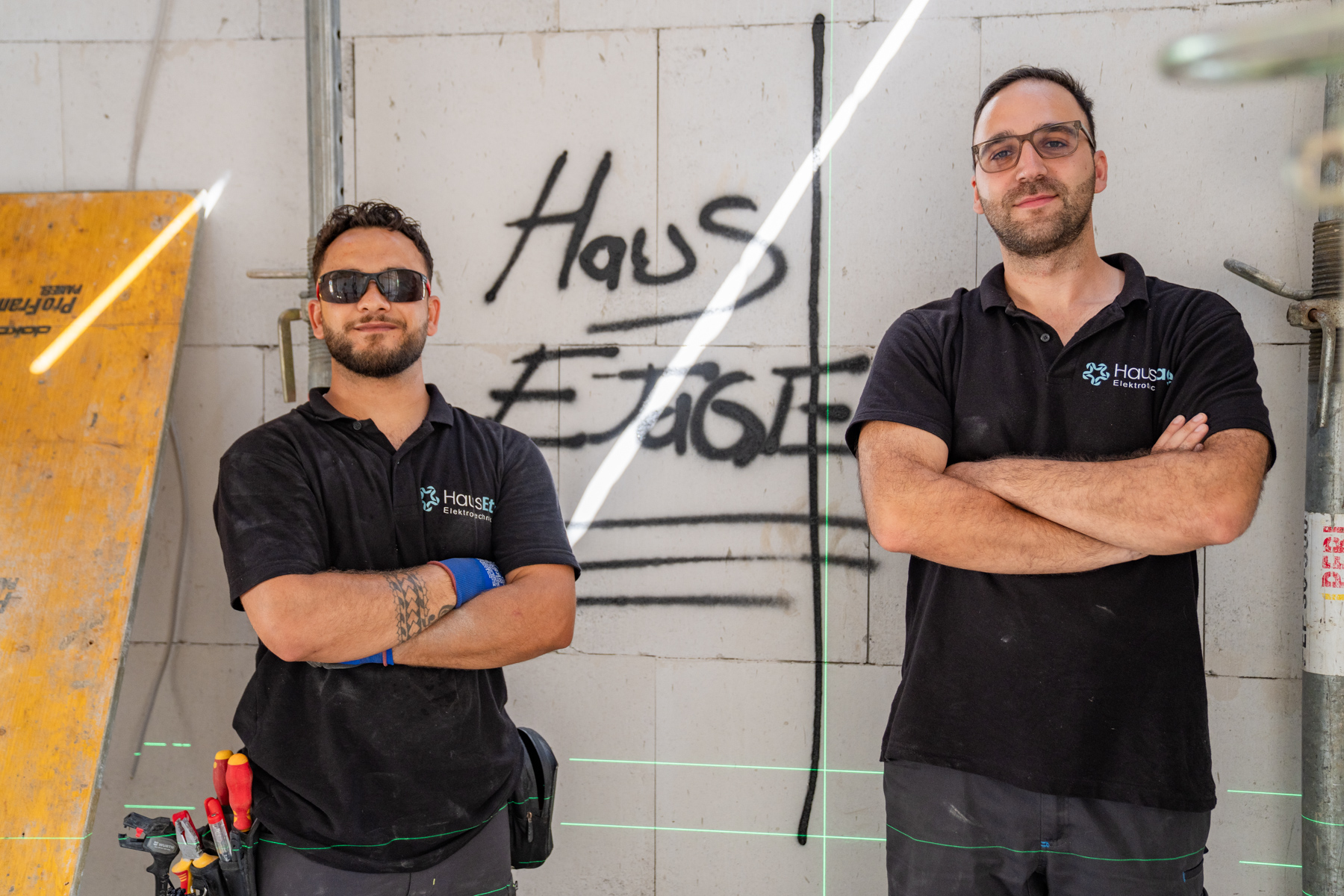 Zwei Elektriker von HausEtage vor einer Wand mit HausEtage-Schriftzug